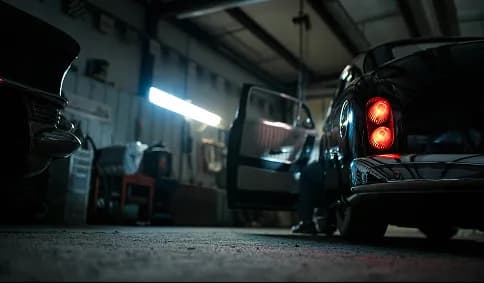 A technician looking under a car in a dim workshop