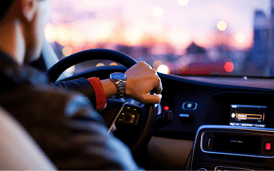 A driver's hand on the steering wheel at dusk