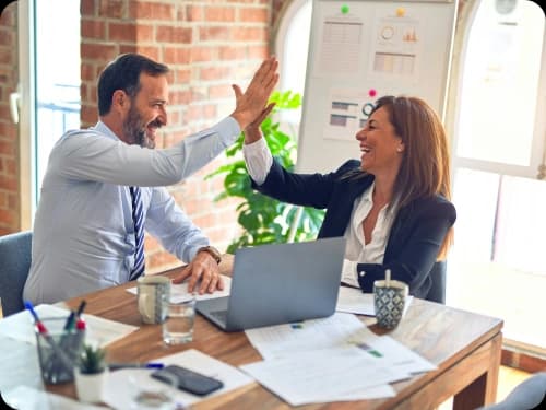 Two colleagues celebrating with a high five at a desk