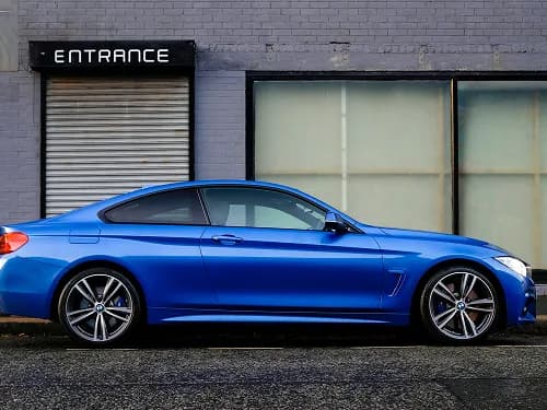 A blue coupé parked outside a building, ready for collection