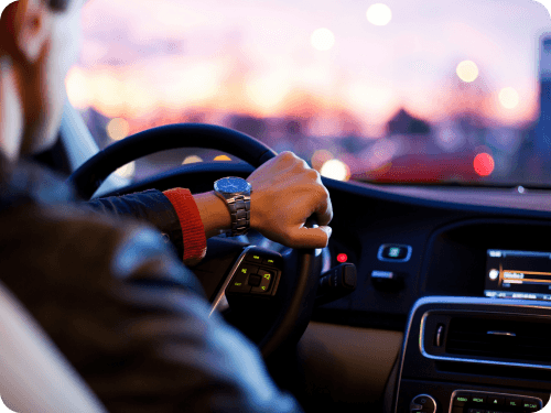 A driver's hand on the steering wheel at dusk